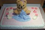 brown teddy bear sitting on pink baby shower cake with blue blanket
