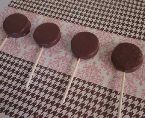 wax paper with white and chocolate covered oreo lollipops sprinkled with colored sprinkles