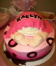 mod mom pink and black polka dot cake with baby bottom with white ruffled underwear showing underneath a pink blanket