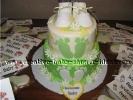 green and yellow cake with green footprints and white baby booties surrounded by favors