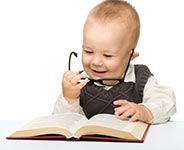 baby in a sweater smiling at a book while holding glasses