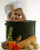 cute baby sitting in a cooking pot surrounded by vegetables wearing chefs hat