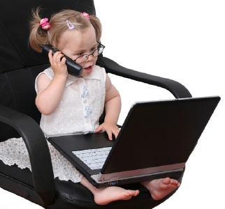busy little girl with cell phone and laptop sitting in business chair