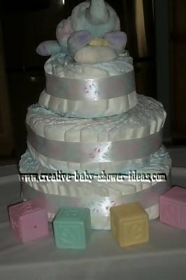 soft white boutique swirl diaper cake with white satin ribbon elephant and baby blocks