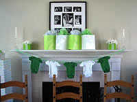 picture taken at a baby shower with a white fireplace with green and white onesies on a clothesline in front and green and white gift bags on top