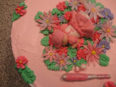 pink cake with flowers and sleeping baby that is wearing pink softball outfit
