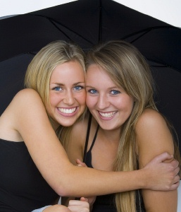 two smiling friends huddled up under a large black umbrella