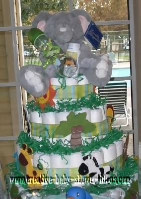 jungle diaper cake with wooden jungle animal cut outs and stuffed elephant on top. green shred paper used on layers