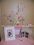 pink table with signed picture of baby sonogram and a white painted tree with baby items tied to it