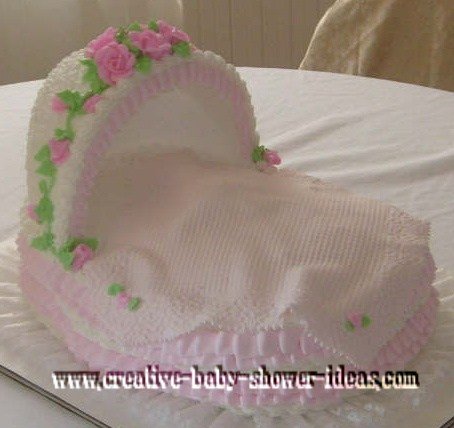 pink and white bassinet cake with flowers and blanket