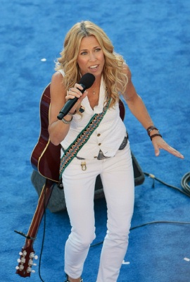 sheryl crow in white suit singing on blue stage