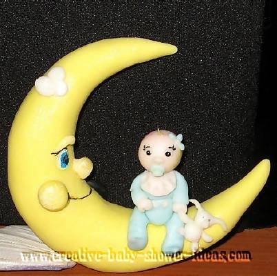 top of moon baby cake with baby wearing blue sleeper sitting on top