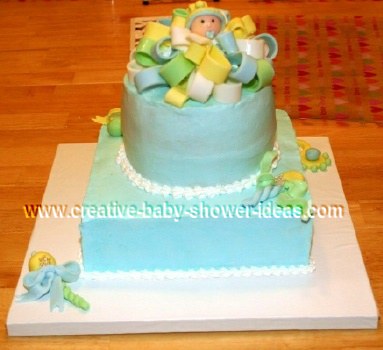2 tier baby boy cake with fondant bow on top and baby boy with pacifier