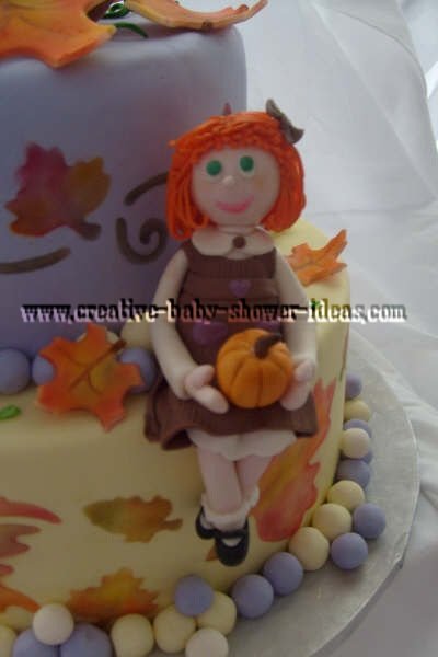 closeup of fall baby shower cake with red headed little girl with brown dress and and pumpkin sitting on cake