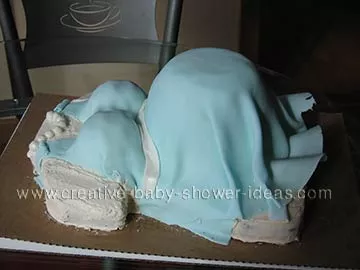 sideview of a pregnant belly cake with blue dress and pearls